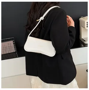 Detail of minimalist cream leather underarm bag with gold knot hardware and slim strap