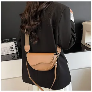 Detail of a brown saddle bag with a wavy flap and a wide canvas strap on a model