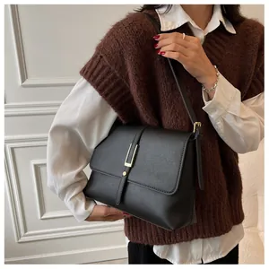 Detail of a vintage black leather shoulder bag with a gold buckle worn by a model