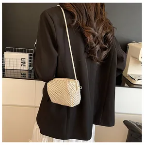 Detail of cream woven mini crossbody bag with fine straw texture and gold zipper closure