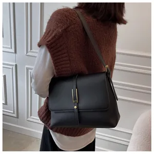 Detailed view of black vintage leather shoulder bag with gold metal buckle on model