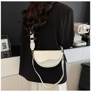 Detail of a beige leather saddle bag with wave-edge flap and golden metal hardware
