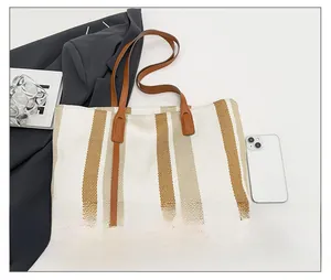Detailed close-up of striped canvas tote bag with brown leather handles and textured fabric