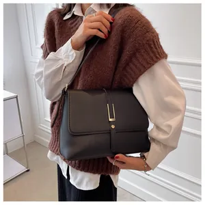 Close-up of a black faux leather shoulder bag with a gold buckle worn by a model