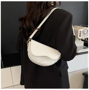 Detail of off-white half-moon saddle bag with wavy edge design and gold hardware
