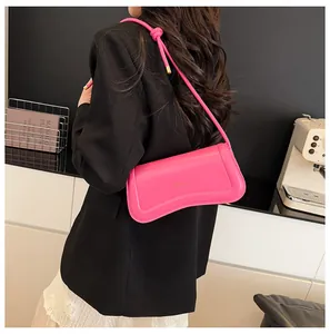 Close-up of bright pink underarm bag featuring curved bottom and gold brand logo