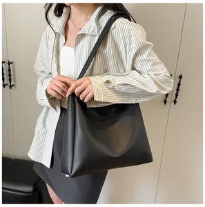 Detailed view of a minimalist black faux leather tote bag worn by a model in a modern room