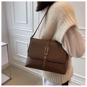 Detail view of vintage dark brown leather shoulder bag with gold buckle on white wall