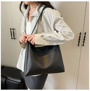 Minimalist black leather tote bag shown on shoulder in a realistic lifestyle setting