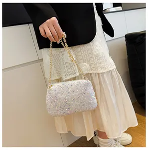 Close-up of elegant white sequin bucket bag with thick gold chain strap held by model
