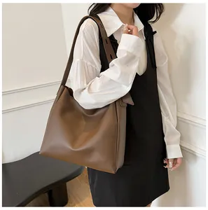 Detail view of a large dark brown faux leather tote bag worn by a model in a minimalist room