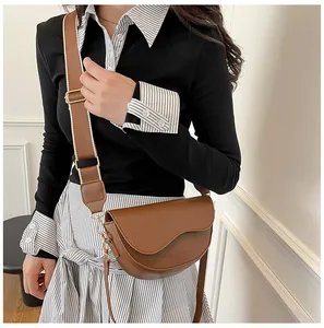 Detail of brown matte leather saddle bag featuring a wide woven strap and gold metal hardware