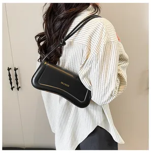 Detail of a minimalist black underarm bag with gold logo and adjustable knotted strap