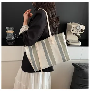 Detailed view of large canvas tote bag with green stripes and white tassels on shoulder