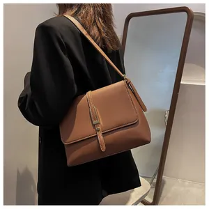 Detail shot of a brown leather shoulder bag with gold metal buckle on a model in a black blazer