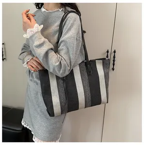 Detailed side view of the large striped canvas tote bag worn by a model in a minimalist room