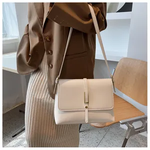 Detailed view of a cream-colored minimalist crossbody bag with a gold metal bar buckle