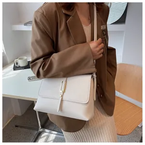 Chic beige crossbody envelope bag with metallic clasp worn with a brown blazer