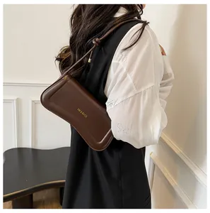 Detail of dark brown leather baguette bag with knotted strap and gold logo
