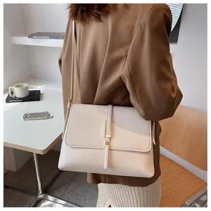 Detail of a minimalist beige leather crossbody bag with gold metal buckle on a model