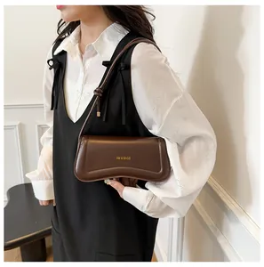 Detail of a coffee brown matte leather underarm bag with gold logo on a female model