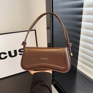 Modern dark brown matte leather baguette bag with knotted strap shown in hand