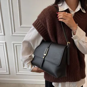 Retro black leather shoulder bag with gold buckle worn by model in a stylish setting