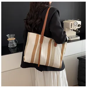 Detailed view of the striped canvas tote bag with brown leather straps on a female model