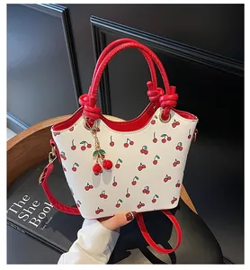 Détail du sac seau à imprimé cerise blanc avec bandoulière rouge et breloque cerise