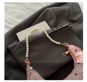 Detail of pink pleated handbag featuring elegant faux pearl handle and gold zipper