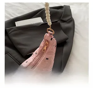 Detail of smooth gold zipper and pearl strap on pink bow print crescent bag