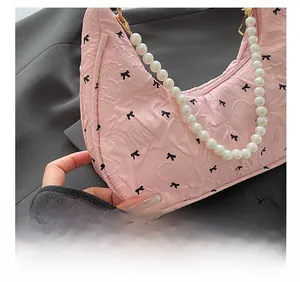 Close-up of pink crescent bag with bow patterns and decorative faux pearl handle strap