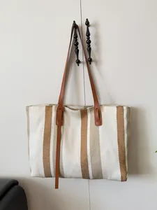 Vertical striped woven tote bag with brown leather straps hanging on a white cabinet door