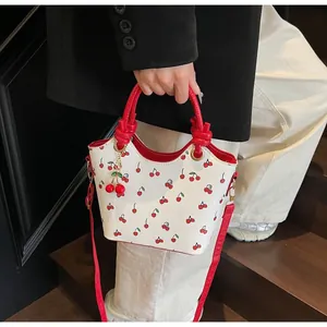 Détail du sac seau blanc avec imprimé cerises et poignée décorative à nœuds rouges
