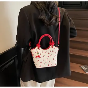 Gros plan d'un sac cabas rétro à motif cerises porté par un mannequin près d'un escalier