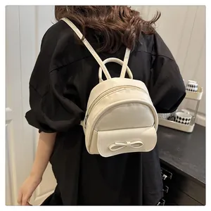 Mini cream bow backpack with smooth faux leather texture shown on person