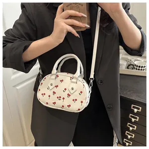 Detail view of the cherry print pattern and leather texture on a white crossbody bag