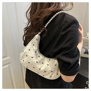 Chic white half-moon bag with black bow embroidery and pearl strap worn by a model