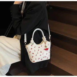 Détail du sac seau blanc à imprimé cerises avec breloque 3D sur un escalier en bois
