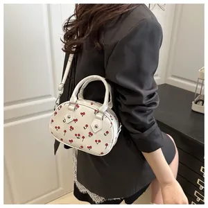 Close-up of white Boston bag with red cherry prints and detachable shoulder strap