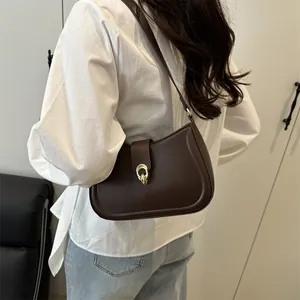Elegant dark brown crescent underarm bag with gold clasp shown on a model's shoulder