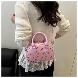 Close-up of pink cherry print handbag styled with a cream knit sweater on a model