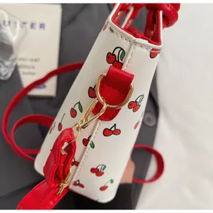 Détail des ferrures dorées et bandoulière rouge du sac seau à motif cerise