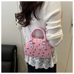 Close-up of light pink Boston bag with cherry prints shown on shoulder with a white sweater