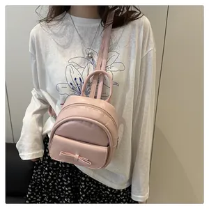 Close-up of pink mini backpack with bow detail worn by a model against a plain wall