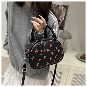 Detail of a black handbag with red cherry patterns featuring silver metal hardware