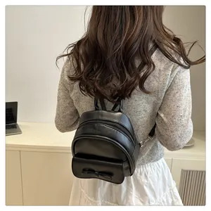 Rear view of model wearing a mini black leather backpack with a decorative bow detail