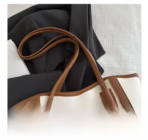 Close-up of the elegant brown leather handle and stitching detail on the contrast tote bag