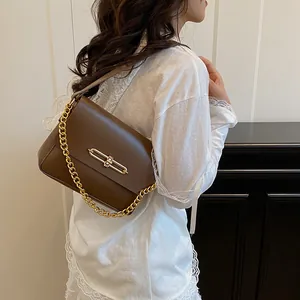 Sac à bandoulière en cuir marron avec chaîne dorée et boucle sur fond ivoire épuré