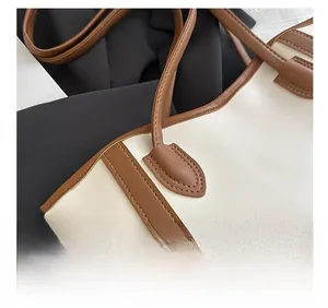 Close-up of contrast stitching and brown leather handle on a cream tote bag